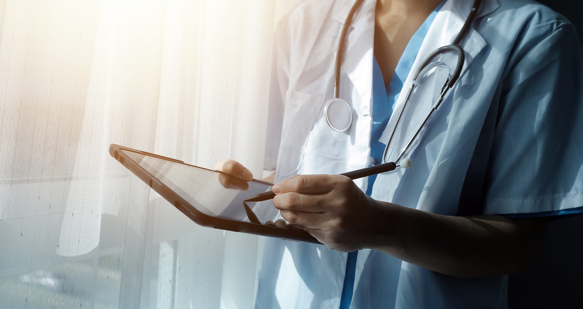 Clinician in scrubs using a tablet in a hospital corridor