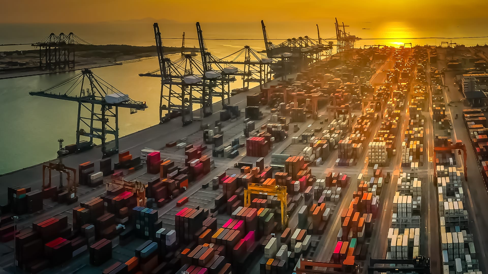 Container terminal with cranes and stacked containers at sunset