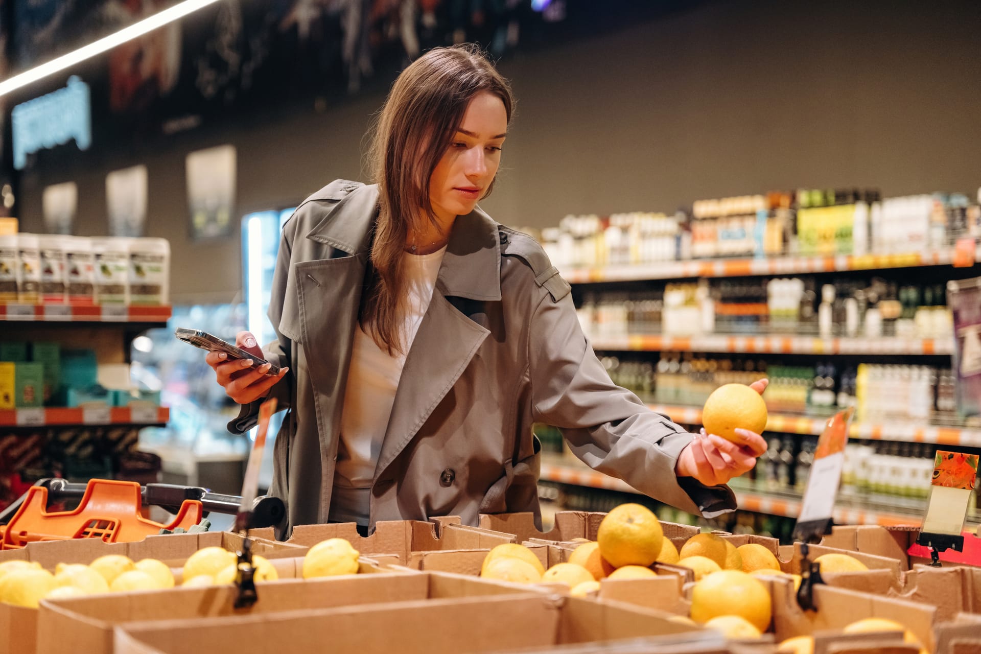 Shopper checking her phone while picking fruit in a grocery store
