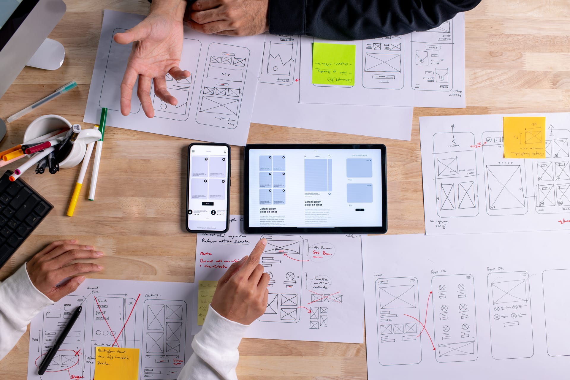 Designers reviewing app wireframes and a tablet prototype at a desk